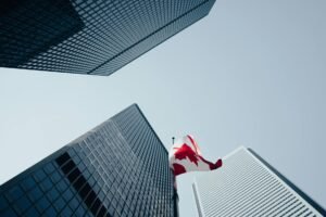 Dramatic low-angle view of skyscrapers and a Canadian flag in downtown Toronto, under a clear blue sky.