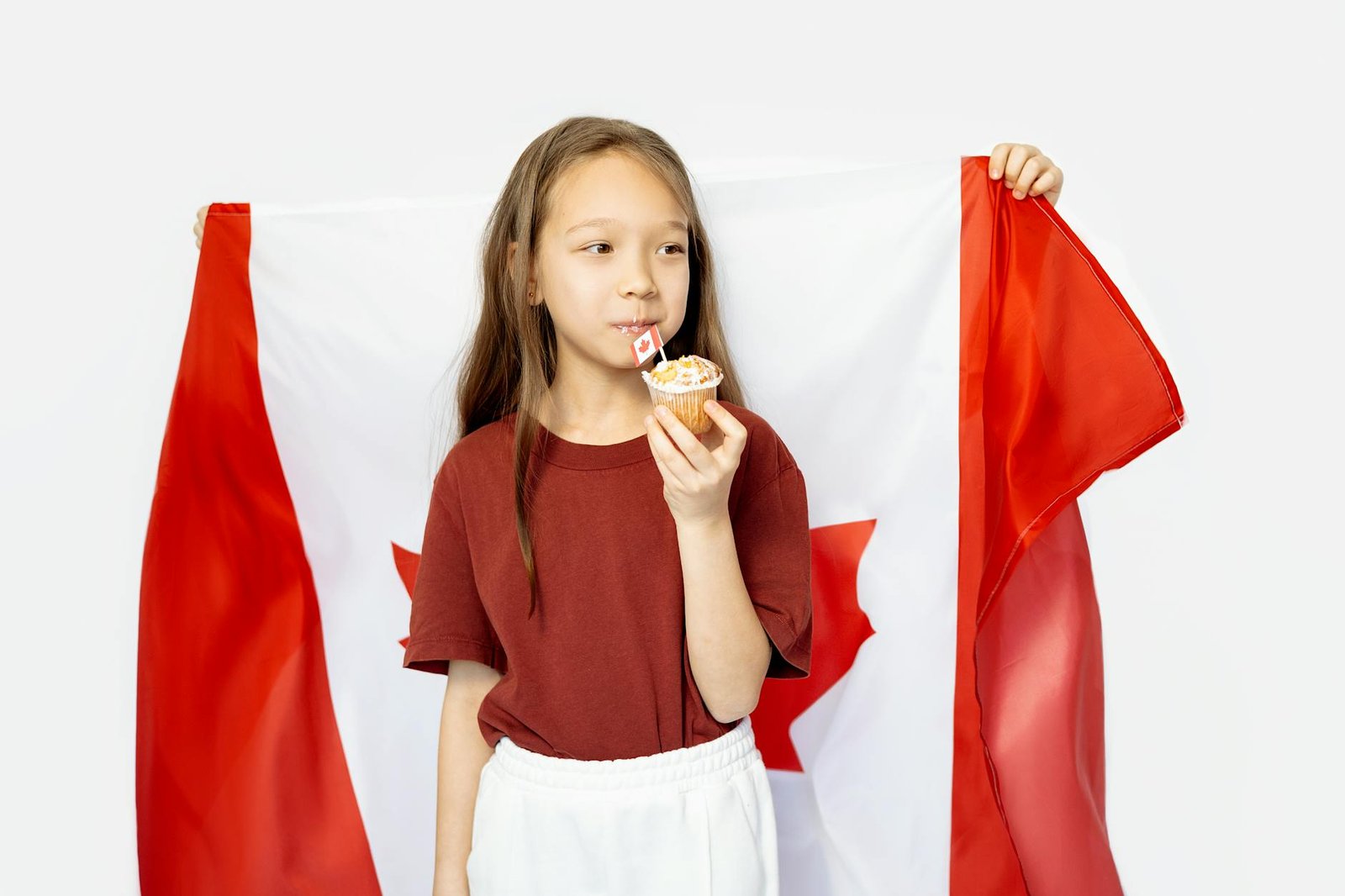 Adorable girl holding a cupcake and Canadian flag, celebrating national pride and delicious treats.
