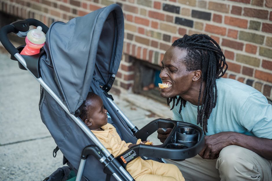 A joyful father engages playfully with his baby in a stroller outdoors.