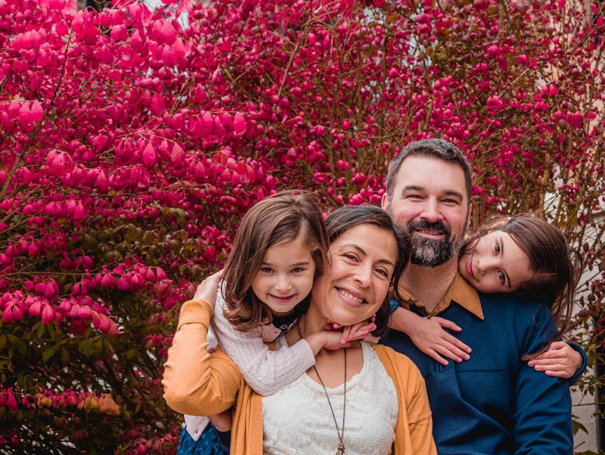 Happy family posing together with pink blossoms in a vibrant garden setting.