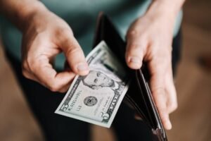 Closeup of crop male in casual clothes taking dollars out of wallet while paying in shop