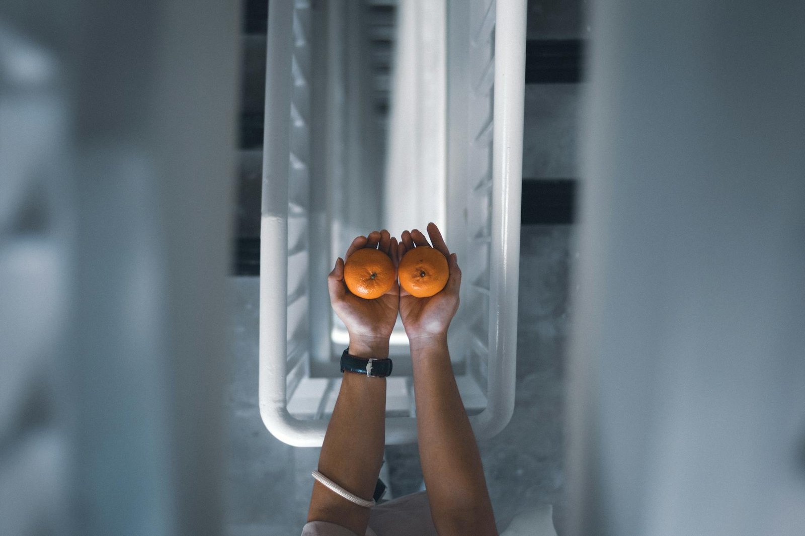 Hands holding two tangerines above a modern staircase, showcasing symmetry and contrast.